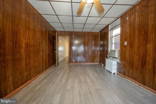 unfurnished living room featuring a paneled ceiling, radiator, ceiling fan, light hardwood / wood-style floors, and wood walls