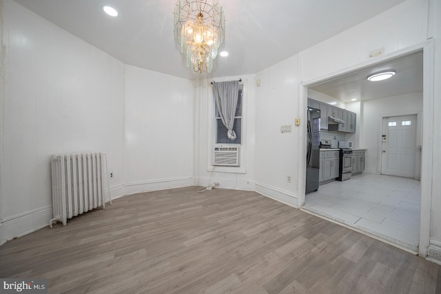 spare room with radiator, light hardwood / wood-style flooring, cooling unit, and a chandelier