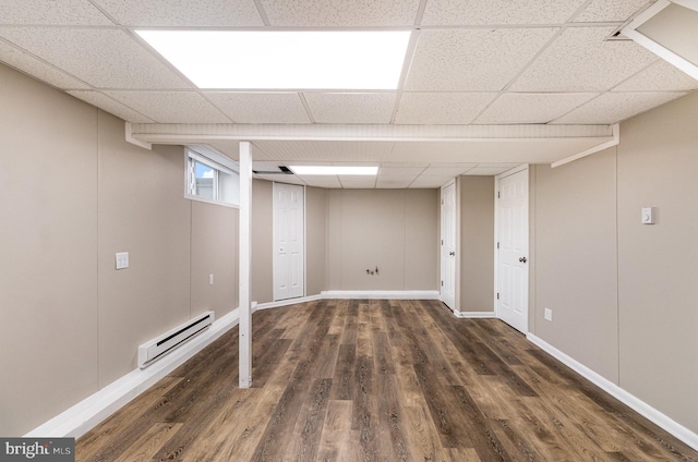 basement featuring a paneled ceiling, dark hardwood / wood-style floors, and baseboard heating