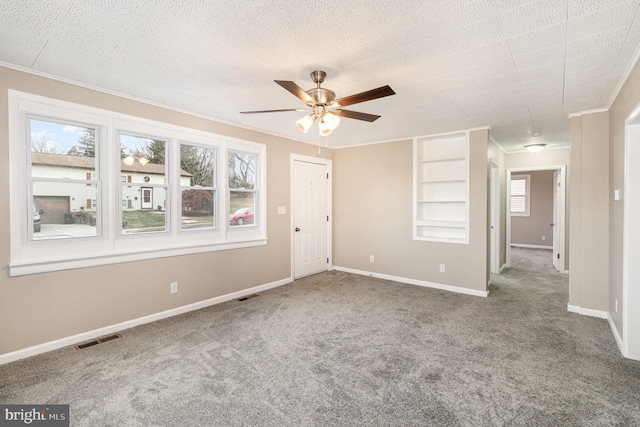 carpeted spare room featuring built in features, plenty of natural light, and ceiling fan