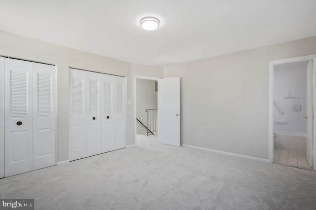 unfurnished bedroom featuring two closets, light colored carpet, and ensuite bath