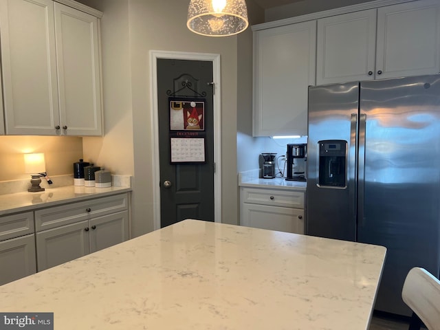 kitchen with light stone countertops, white cabinets, decorative light fixtures, and stainless steel refrigerator with ice dispenser