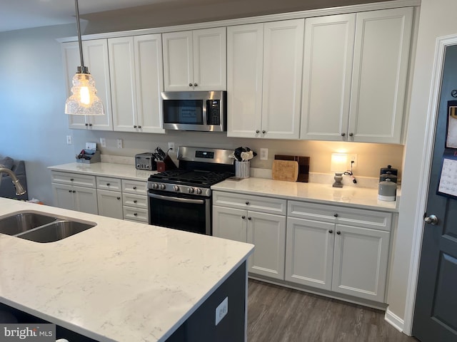 kitchen with sink, dark wood-type flooring, pendant lighting, white cabinets, and appliances with stainless steel finishes