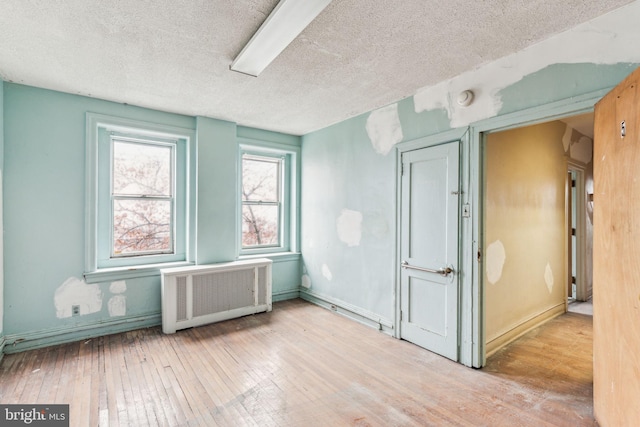 unfurnished room featuring radiator heating unit, a textured ceiling, and light hardwood / wood-style flooring