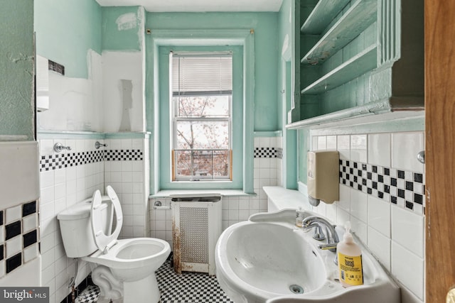 bathroom with radiator, sink, tile patterned flooring, toilet, and tile walls