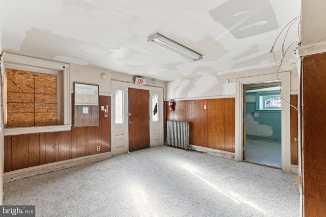 carpeted spare room featuring radiator and wooden walls