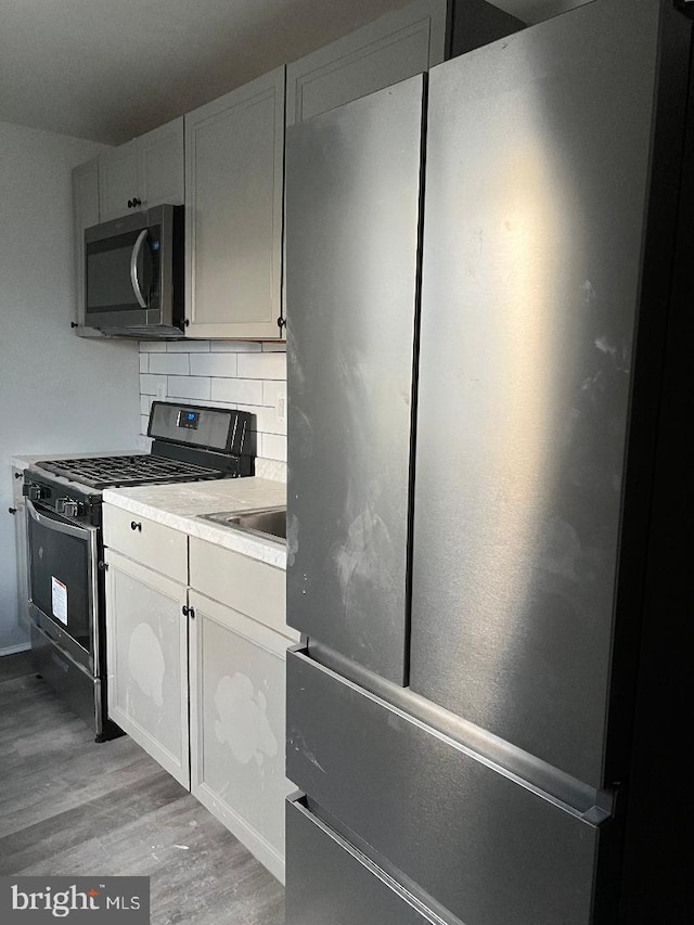 kitchen featuring sink, tasteful backsplash, light hardwood / wood-style floors, white cabinetry, and stainless steel appliances