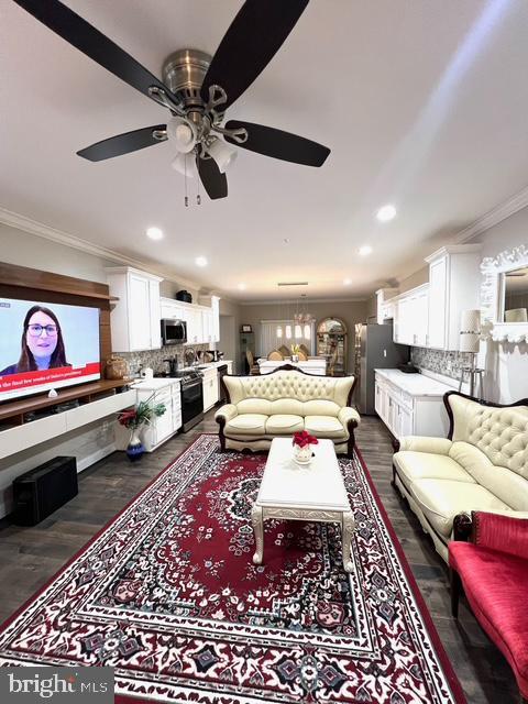 living room featuring crown molding, dark wood-type flooring, and ceiling fan with notable chandelier