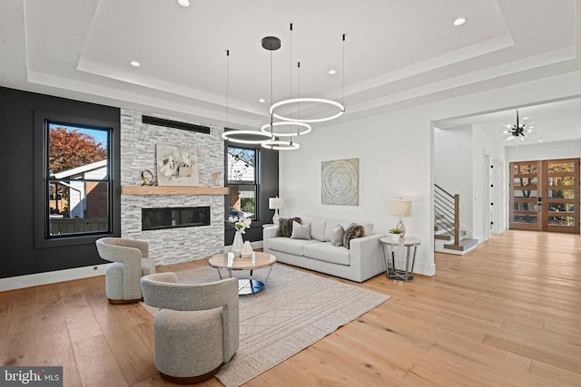 living room with a chandelier, light wood-type flooring, a raised ceiling, and a stone fireplace