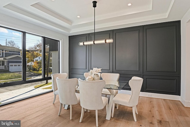 dining room with light wood-type flooring and a raised ceiling