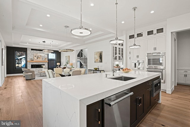 kitchen with a raised ceiling, sink, a center island with sink, and appliances with stainless steel finishes