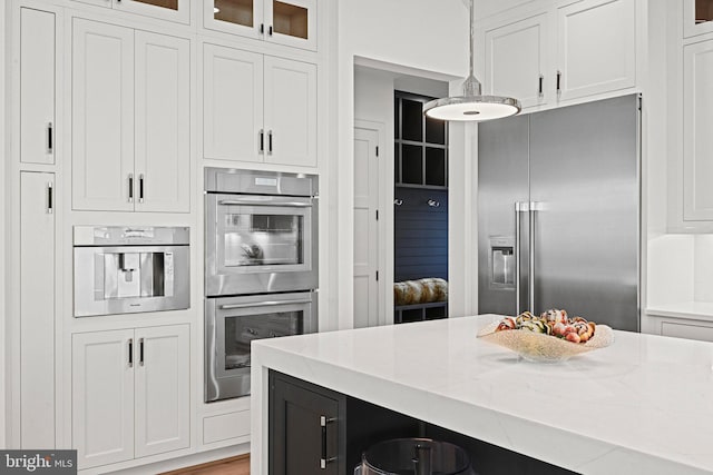 kitchen featuring white cabinets, decorative light fixtures, light stone counters, and appliances with stainless steel finishes