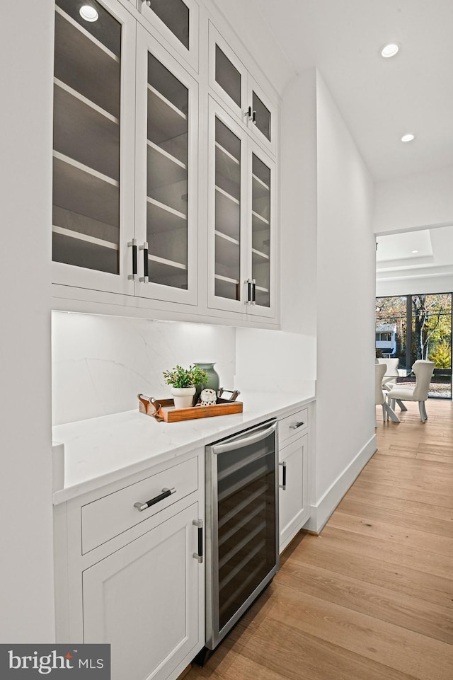 bar featuring white cabinets, decorative backsplash, light stone countertops, light hardwood / wood-style floors, and beverage cooler