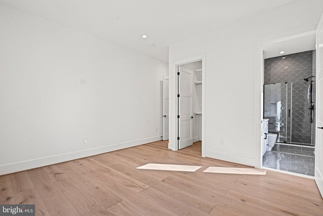 unfurnished bedroom with a walk in closet, ensuite bathroom, and light wood-type flooring