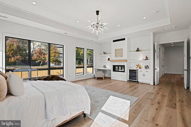 bedroom featuring a chandelier, light hardwood / wood-style floors, wine cooler, and a tray ceiling