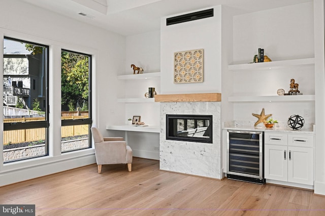 bar with wine cooler, light hardwood / wood-style flooring, white cabinets, and built in features