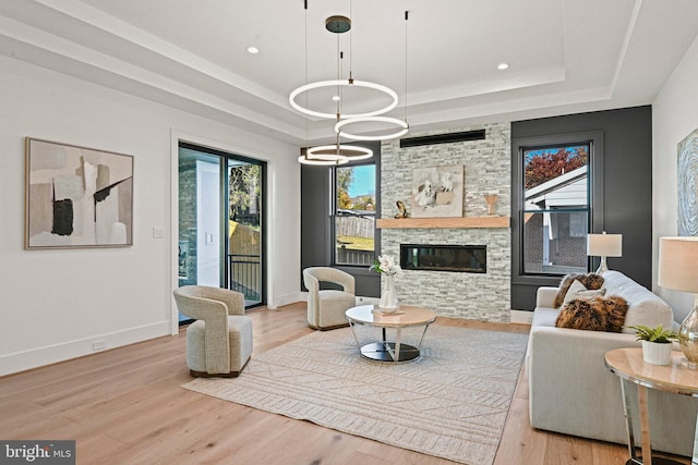 living room featuring a fireplace, a tray ceiling, a chandelier, and light hardwood / wood-style floors