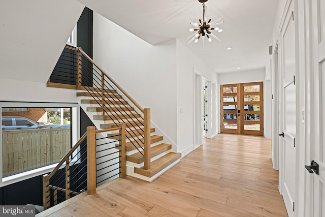 entrance foyer with french doors, light hardwood / wood-style floors, and an inviting chandelier