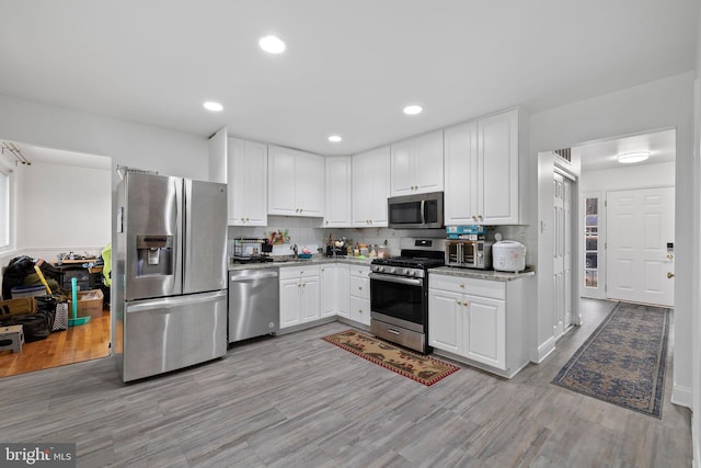 kitchen featuring decorative backsplash, light hardwood / wood-style floors, white cabinetry, and appliances with stainless steel finishes