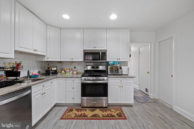 kitchen with white cabinets, sink, stainless steel appliances, and light hardwood / wood-style flooring