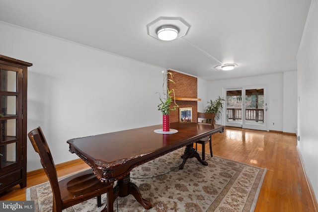 dining room with light hardwood / wood-style floors, a brick fireplace, and crown molding