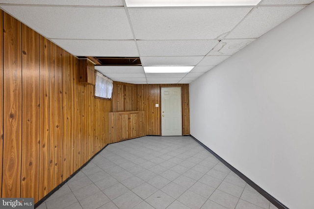 basement featuring wooden walls, a drop ceiling, and light tile patterned flooring