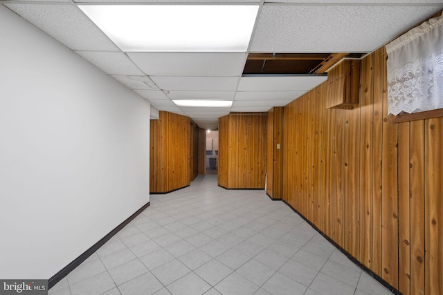 interior space featuring wood walls, a drop ceiling, and light tile patterned flooring