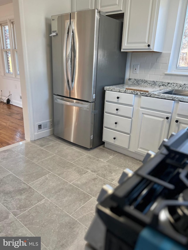 kitchen featuring light tile patterned floors, stainless steel refrigerator, light stone counters, white cabinets, and decorative backsplash