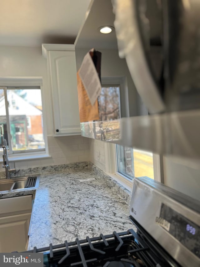 details featuring stainless steel gas range oven, sink, white cabinets, and backsplash