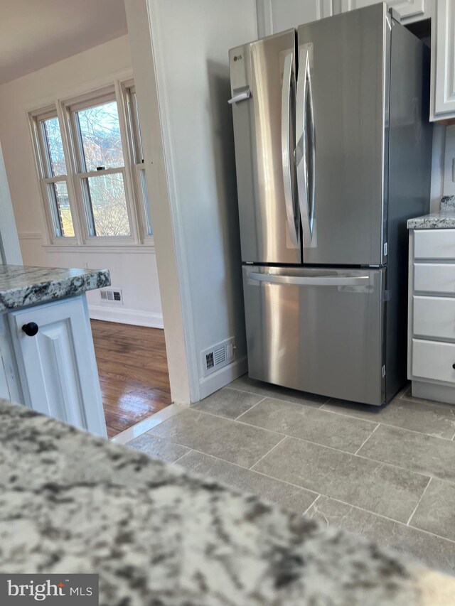 kitchen featuring white cabinetry, light stone countertops, light tile patterned flooring, and stainless steel fridge