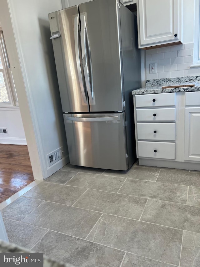 kitchen with stainless steel refrigerator, light stone countertops, tasteful backsplash, and white cabinets