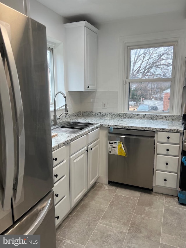 kitchen featuring sink, appliances with stainless steel finishes, tasteful backsplash, light stone countertops, and white cabinets