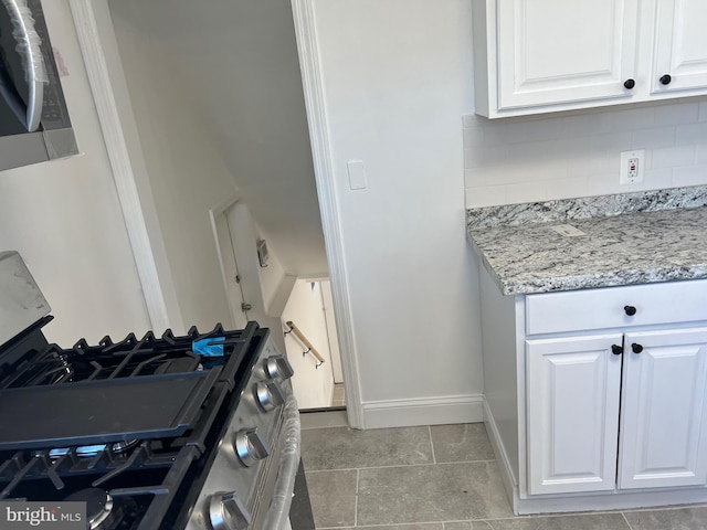 kitchen with white cabinetry, light stone countertops, gas stove, and tasteful backsplash