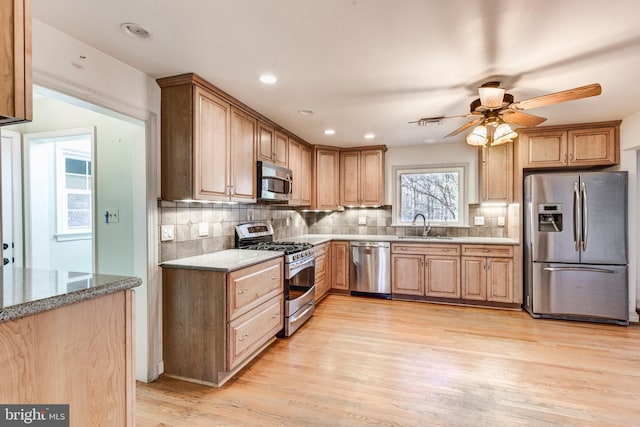 kitchen with sink, decorative backsplash, light stone countertops, light hardwood / wood-style floors, and stainless steel appliances