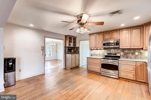 kitchen with ceiling fan with notable chandelier, light hardwood / wood-style floors, appliances with stainless steel finishes, and tasteful backsplash