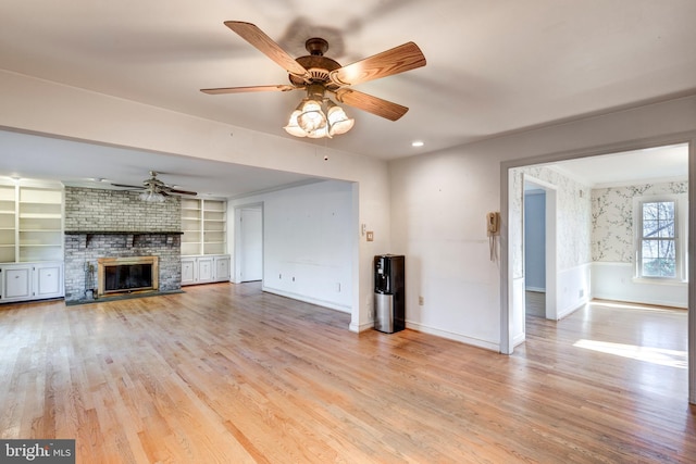 unfurnished living room featuring ceiling fan, built in features, light hardwood / wood-style flooring, and a brick fireplace