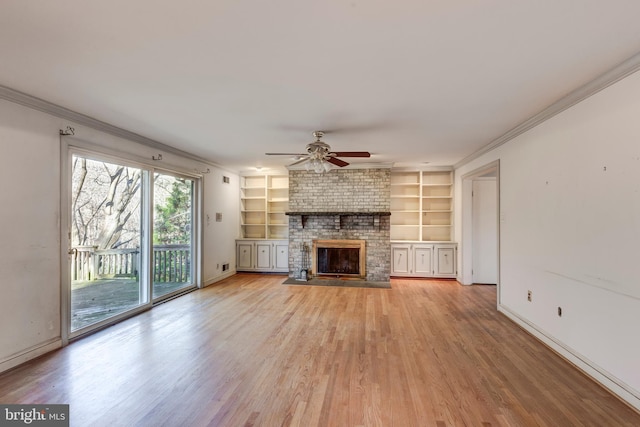 unfurnished living room featuring built in shelves, ceiling fan, a brick fireplace, crown molding, and light wood-type flooring