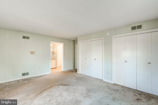 unfurnished bedroom featuring two closets, light colored carpet, and ensuite bathroom