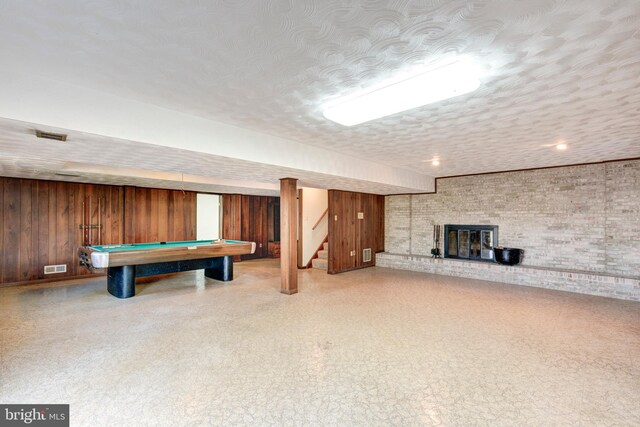 playroom with a brick fireplace, brick wall, a textured ceiling, wood walls, and pool table