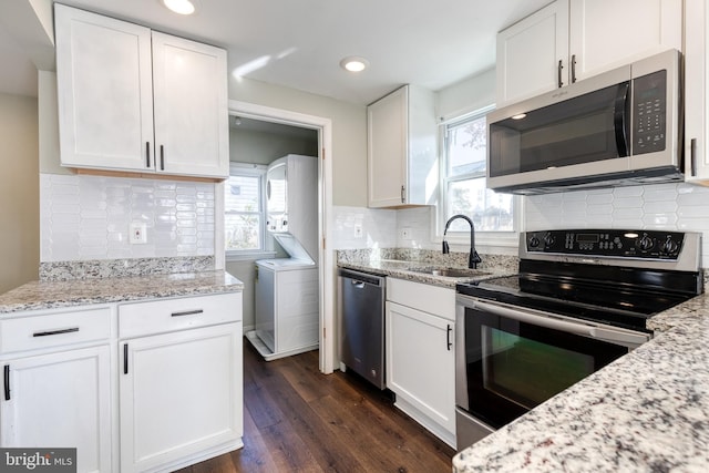 kitchen with appliances with stainless steel finishes, backsplash, stacked washer and dryer, white cabinets, and dark hardwood / wood-style floors