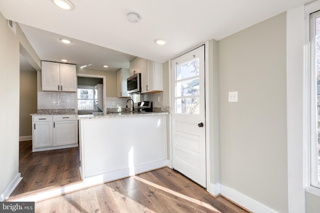 kitchen with white cabinets, hardwood / wood-style flooring, tasteful backsplash, light stone counters, and stainless steel appliances