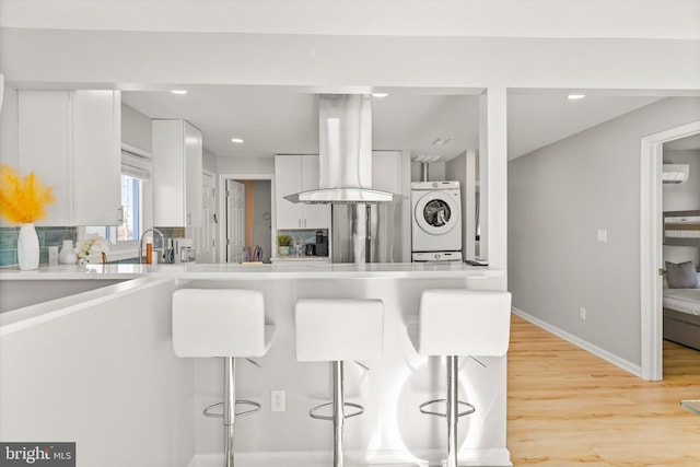 kitchen with a wall mounted air conditioner, white cabinets, light wood-type flooring, island range hood, and a kitchen bar