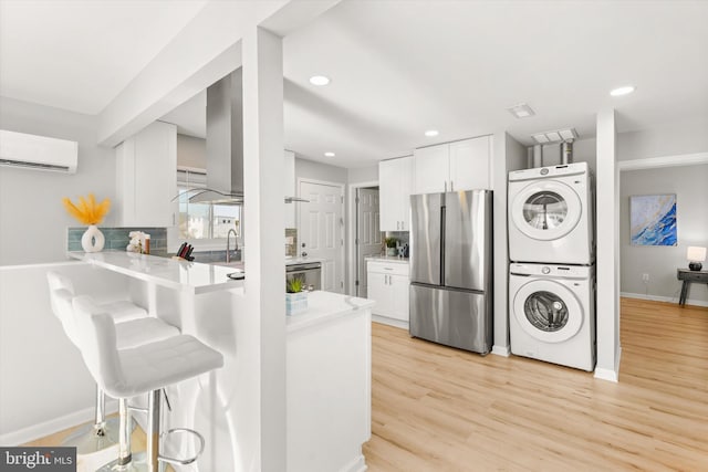 kitchen with white cabinetry, kitchen peninsula, stainless steel fridge, stacked washer and clothes dryer, and light wood-type flooring