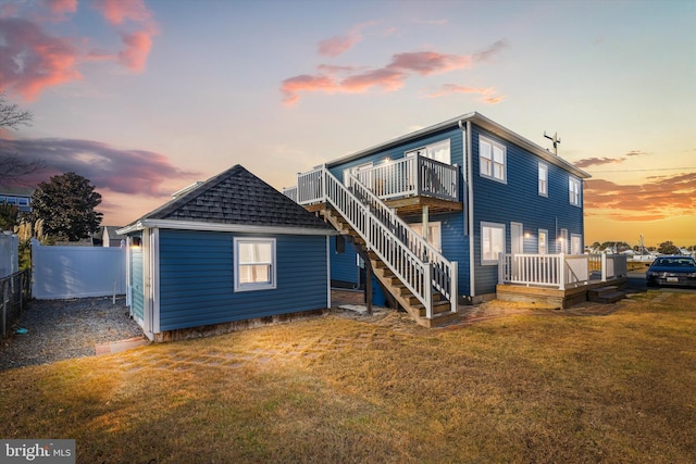 back house at dusk with a wooden deck and a lawn