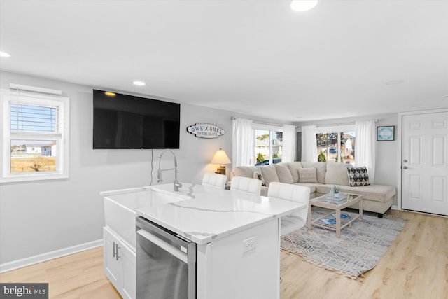 kitchen with white cabinets, dishwasher, an island with sink, and light hardwood / wood-style flooring