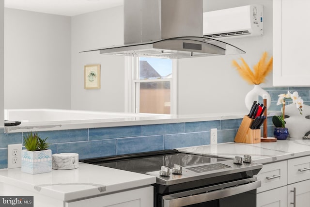 kitchen with tasteful backsplash, light stone counters, a wall unit AC, island range hood, and white cabinets