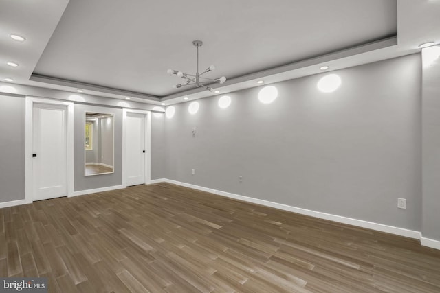 unfurnished room featuring a notable chandelier, a raised ceiling, and wood-type flooring