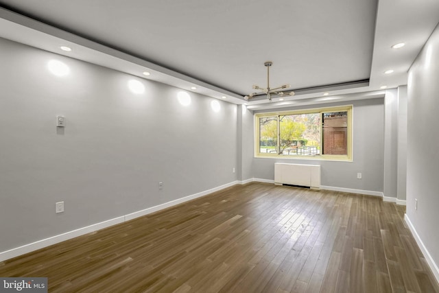 empty room with radiator heating unit, hardwood / wood-style flooring, an inviting chandelier, and a tray ceiling