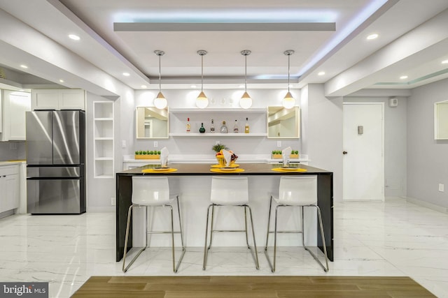 kitchen featuring a kitchen breakfast bar, white cabinetry, stainless steel refrigerator, and a tray ceiling