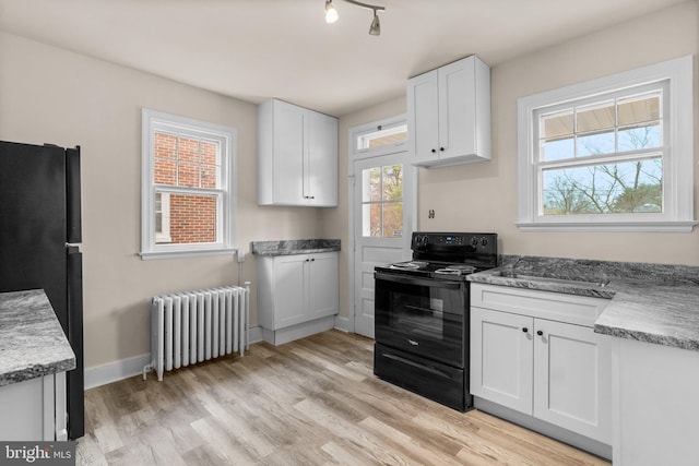 kitchen featuring radiator, black appliances, light wood-type flooring, light stone counters, and white cabinetry